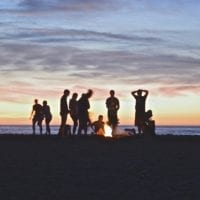 People on the beach at sunset around a campfire.