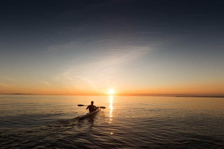 A person in a kayak paddling at sunset