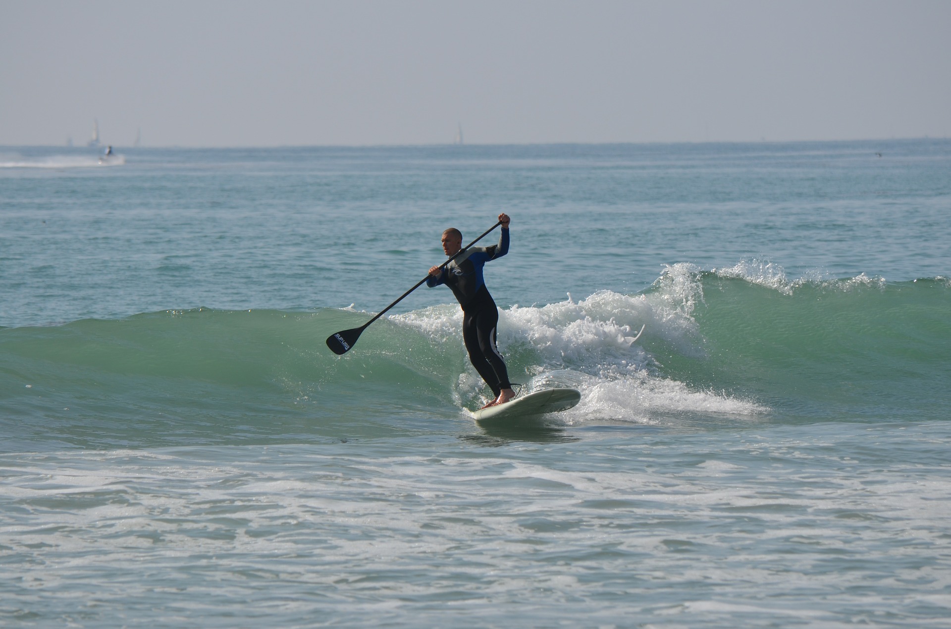 Man riding a wave on a stand up paddle board.