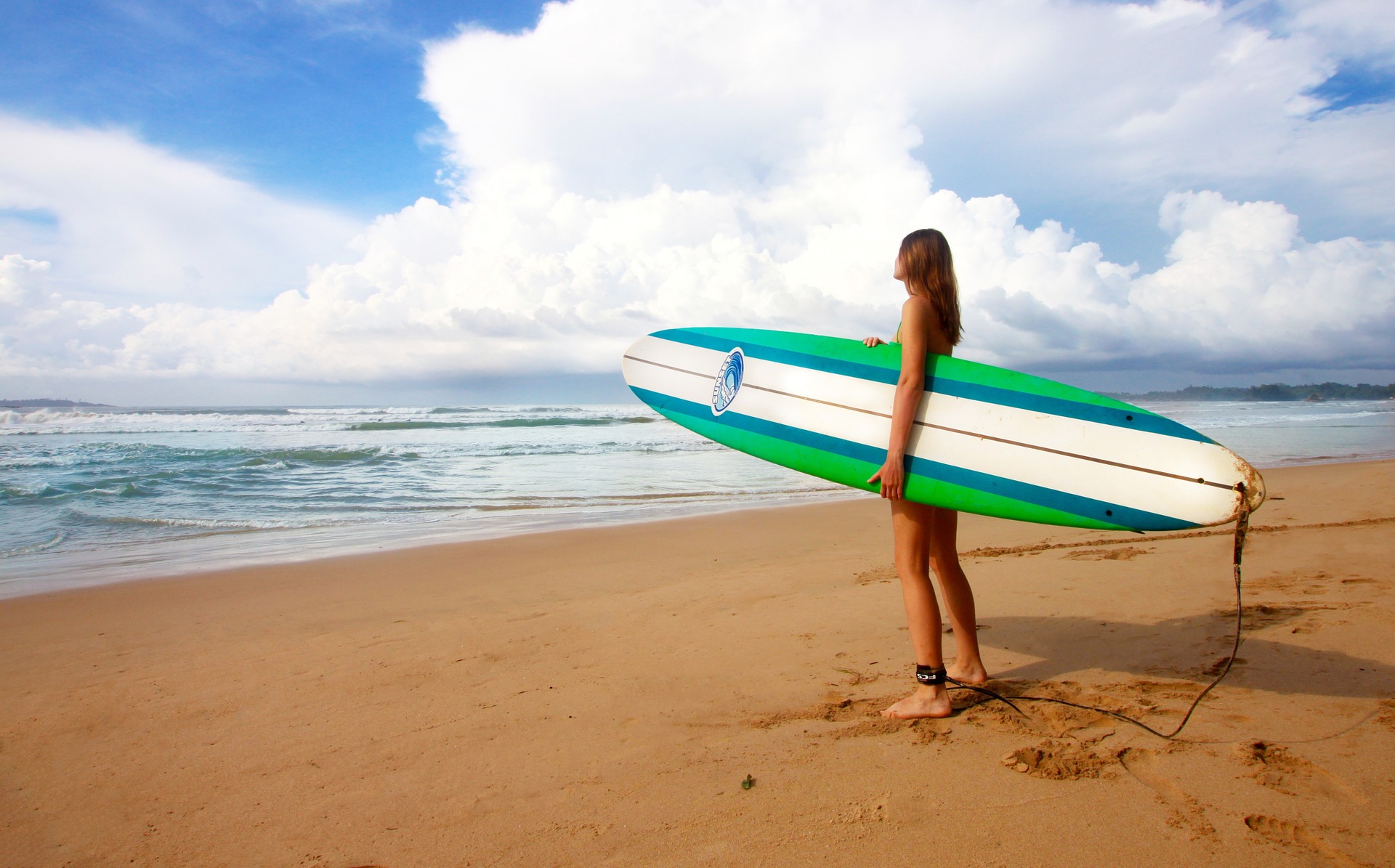 A girl with a colorful surfboard looking at the ocean.